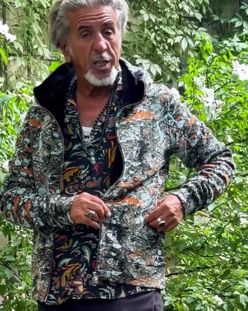 Hamid in der offenen Jacke Nilo mit türkis-orangem Strickmuster, der Schalkragen liegt flach um den Hals, darunter ein gemustertes Hemd
