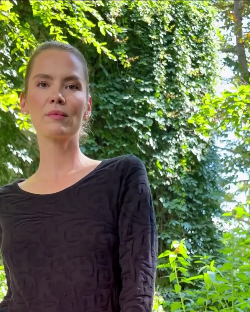 Elisabeth allein im Garten im Strickkleid Nusha mit weiter schwarzer Hose