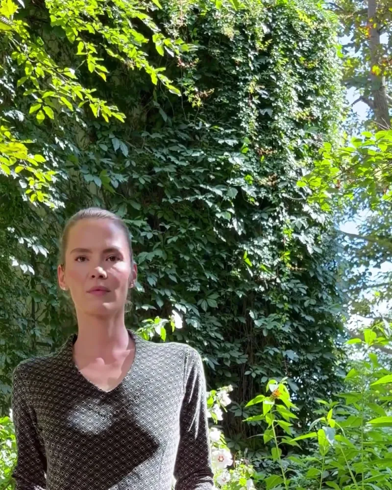 Elisabeth geht im Kleid Daria über einer weiten schwarzen Hose durch den Garten