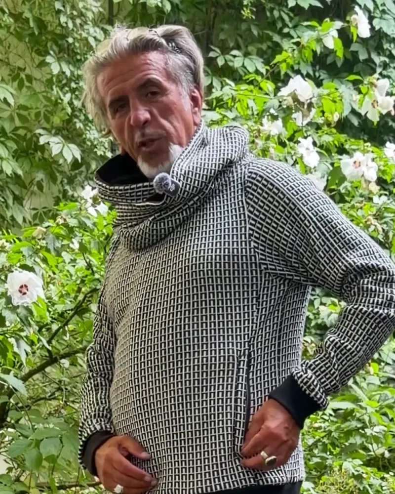 Hamid im schwarz-weiß gemusterten Pullover Nils, die Hand an der Tasche